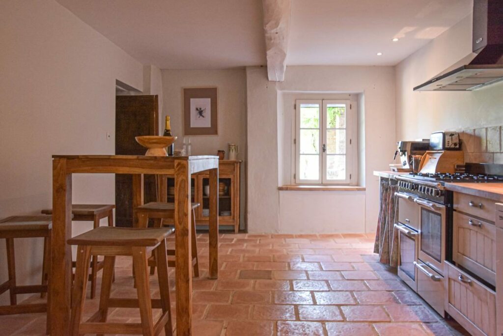 La cuisine : piano de cuisson, table haute avec tabourets et carrelage en terre cuite