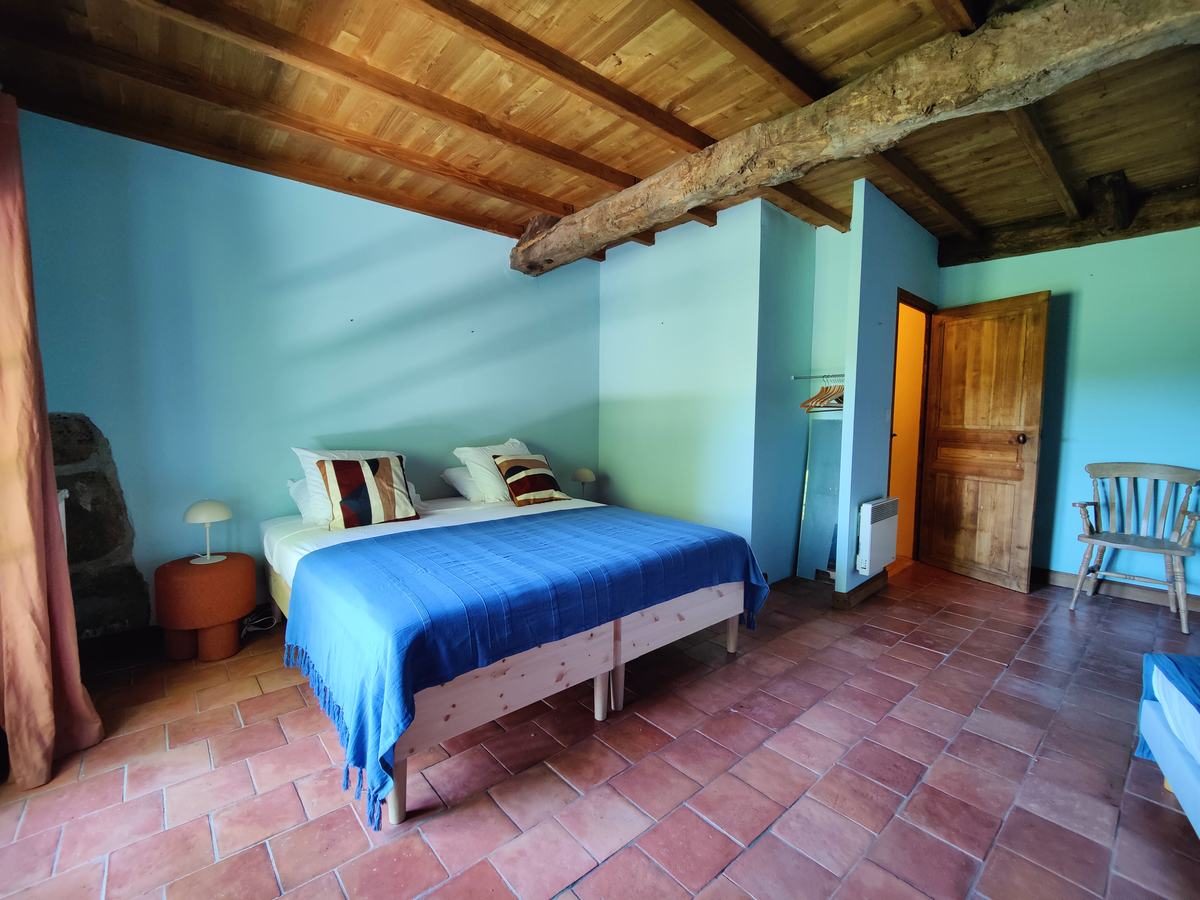 Chambre aux murs turquoise et poutres apparentes, avec un grand lit